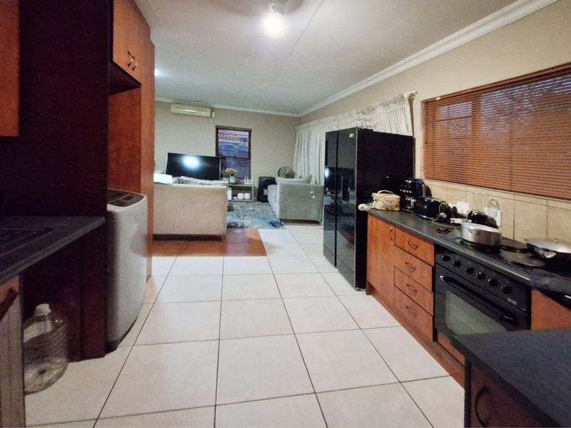 Open-plan kitchen and living area featuring tiled flooring, wooden cabinetry, and an integrated oven, creating a functional and connected living space.