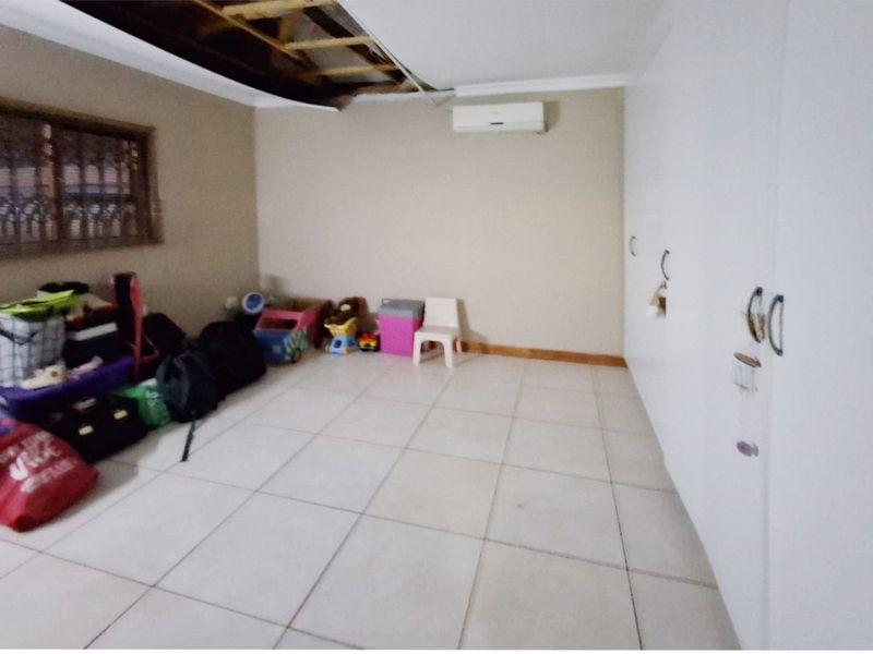 Bedroom featuring tiled flooring, built-in cupboards, and a split-system air conditioner. Note the significant damage to the ceiling requiring repair.