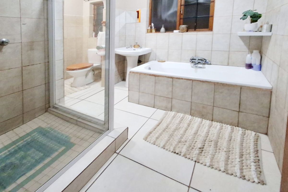 A functional bathroom featuring a pedestal basin, built-in bathtub, and a separate glass-enclosed shower with neutral ceramic tiling throughout.