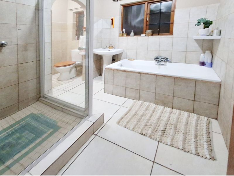 A functional bathroom featuring a pedestal basin, built-in bathtub, and a separate glass-enclosed shower with neutral ceramic tiling throughout.