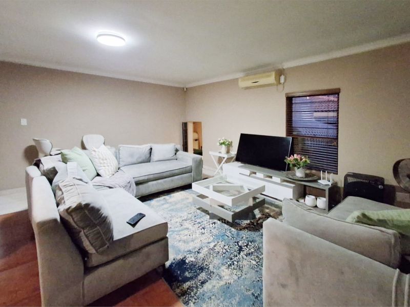 A comfortable living room featuring a wall-mounted split-system air conditioner, neutral wall tones, and window blinds.