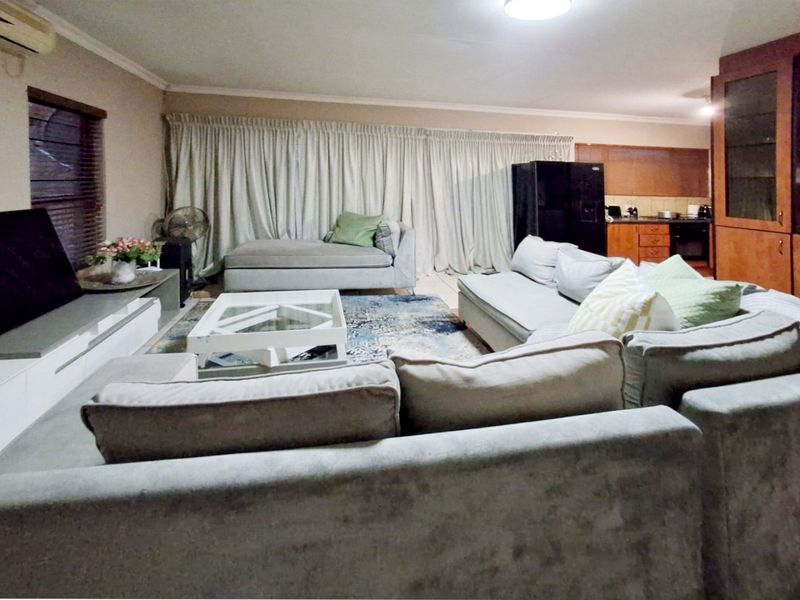 Spacious open-plan living area featuring tiled flooring, integrated kitchen cabinetry, and a wall-mounted air conditioning unit, creating a functional and connected living space.