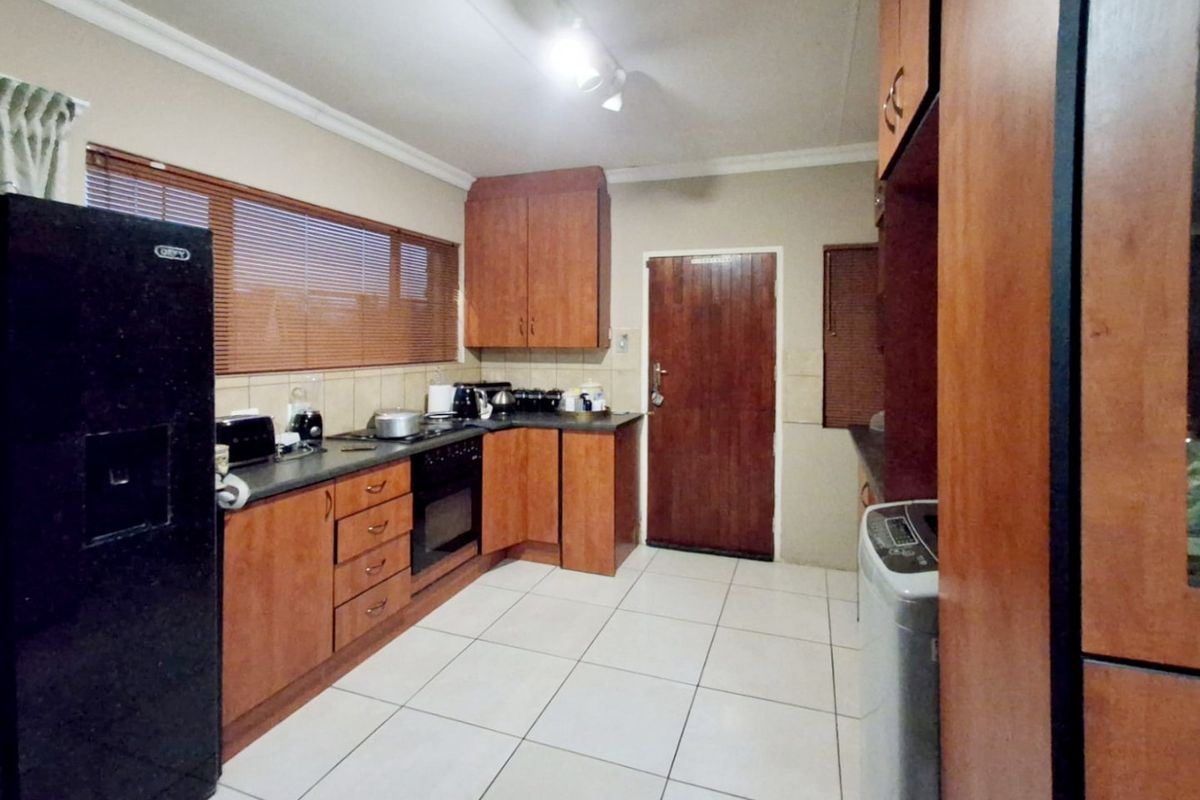 A functional kitchen featuring wooden cabinetry, laminate countertops, built-in oven, hob, and tiled flooring with natural light from the window.