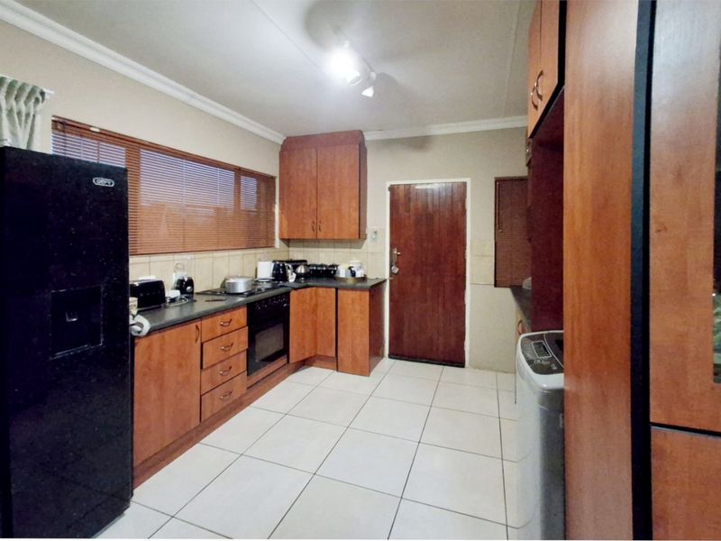 A functional kitchen featuring wooden cabinetry, laminate countertops, built-in oven, hob, and tiled flooring with natural light from the window.