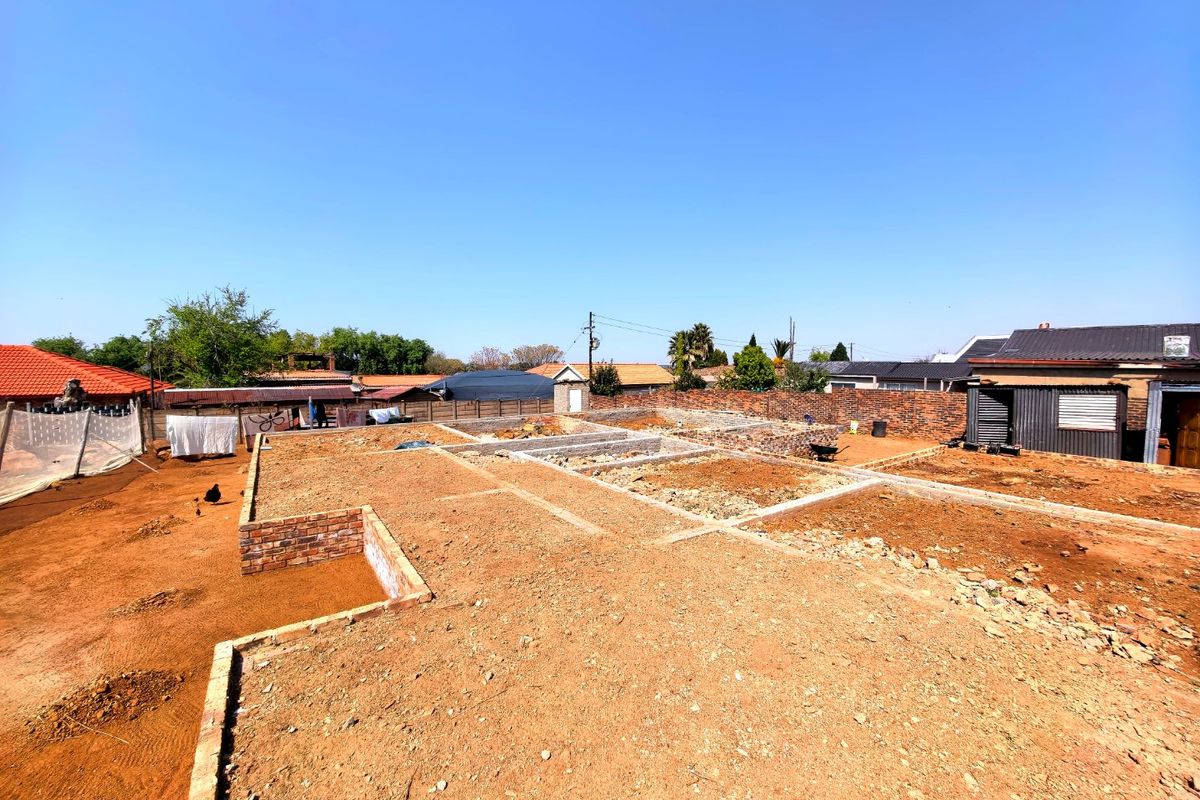 A vacant residential plot showing active construction with brick foundations and concrete footings laid out on the site.