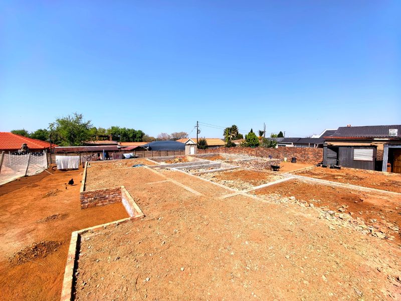 A vacant residential plot showing active construction with brick foundations and concrete footings laid out on the site.