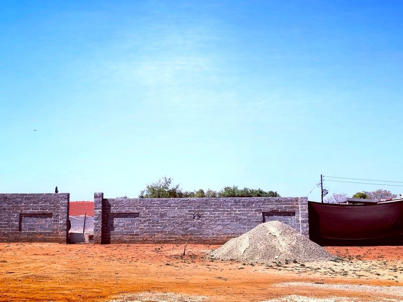 A vacant residential plot featuring a newly constructed perimeter brick wall and piles of construction materials on site.