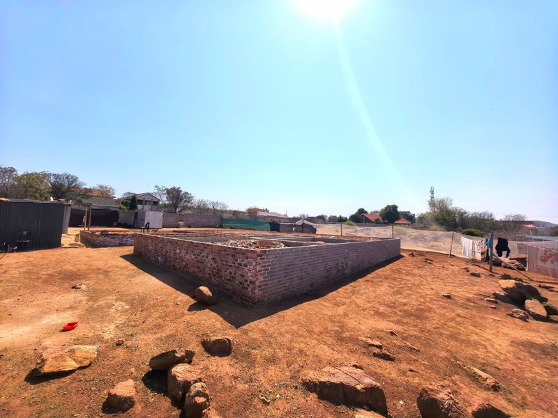 A vacant residential plot featuring an exposed brick foundation for a new building project, set within a fenced perimeter.