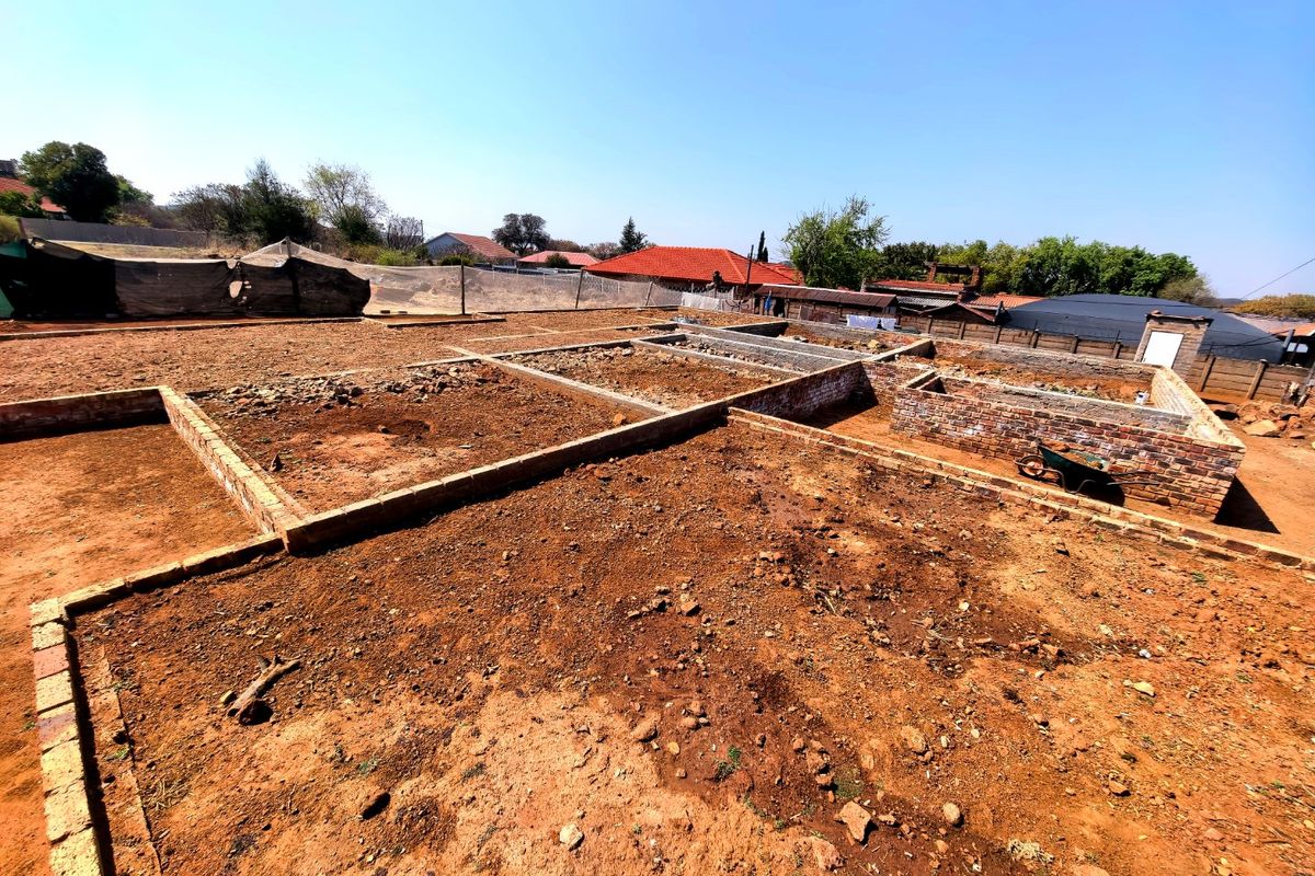 A vacant residential plot featuring an incomplete brick foundation and perimeter wall, offering a blank canvas for future development.