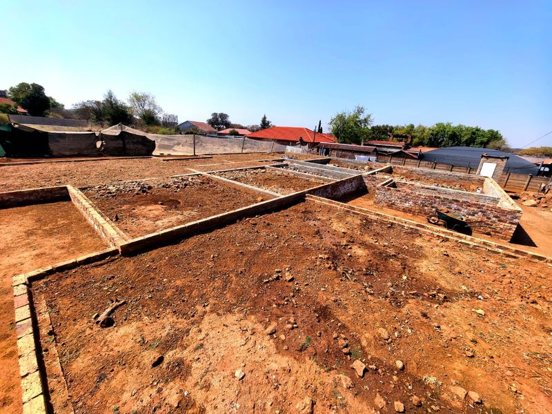 A vacant residential plot featuring an incomplete brick foundation and perimeter wall, offering a blank canvas for future development.