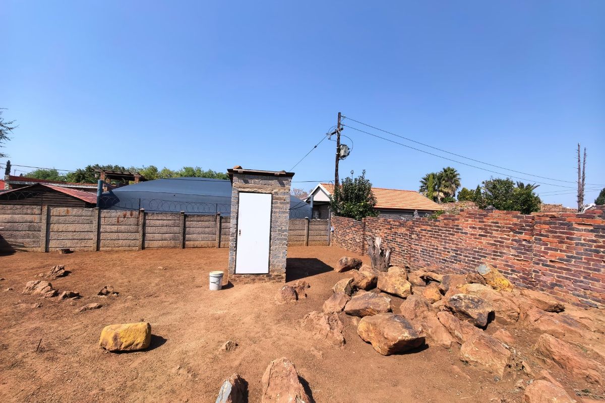 A vacant residential plot featuring a small stone structure, enclosed by brick and precast concrete boundary walls with security razor wire.