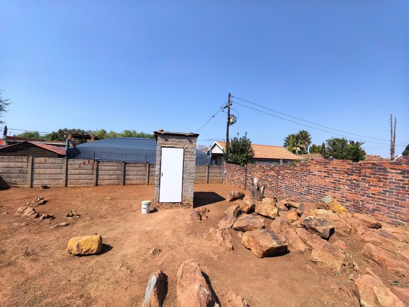 A vacant residential plot featuring a small stone structure, enclosed by brick and precast concrete boundary walls with security razor wire.