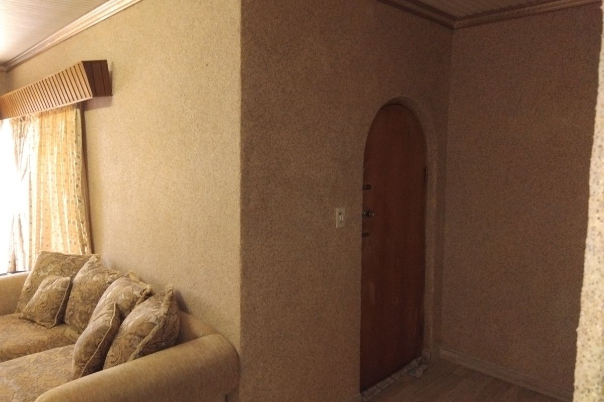 Living room featuring dated textured wall finishes, an arched doorway, and traditional crown molding, offering potential for a modern interior update.