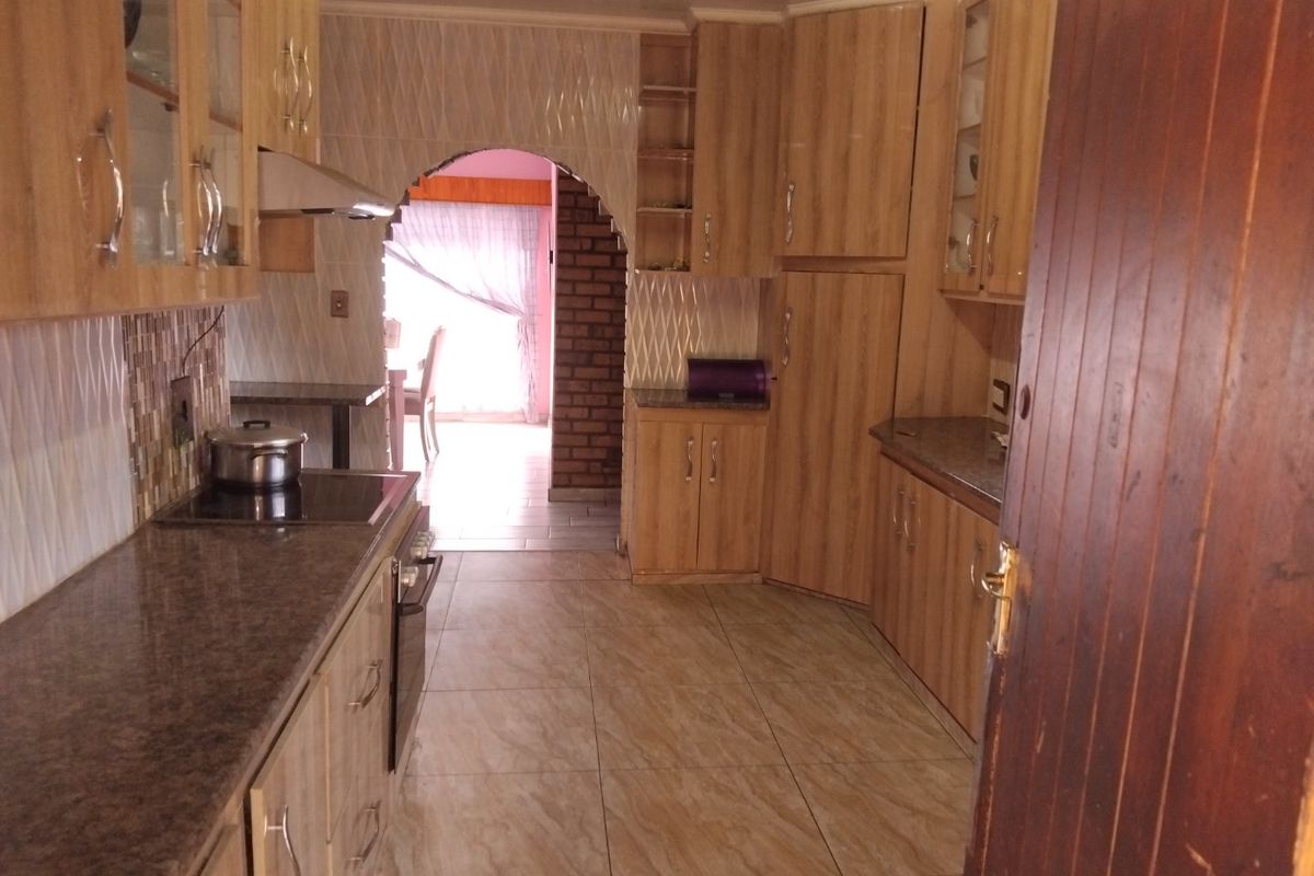 A functional kitchen featuring wood-look laminate cabinetry, granite countertops, built-in cooking appliances, and tiled flooring, leading through an archway to an adjacent living area.