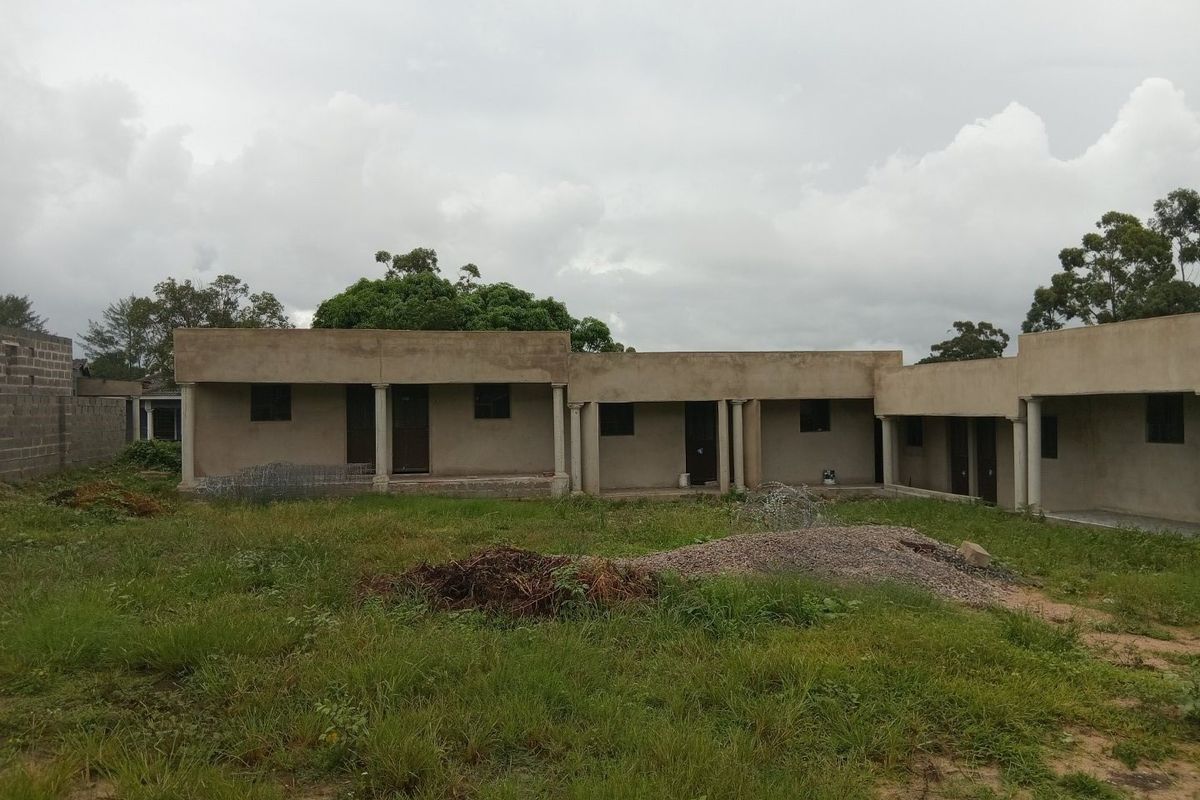 Rear view of a single-story apartment building featuring a covered veranda with concrete columns, currently in an unfinished state with surrounding unlandscaped grounds.