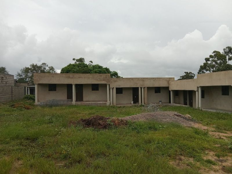 Rear view of a single-story apartment building featuring a covered veranda with concrete columns, currently in an unfinished state with surrounding unlandscaped grounds.