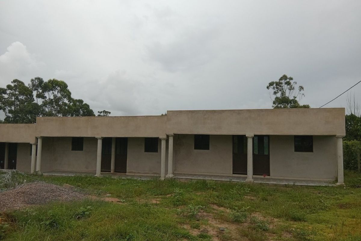 Exterior view of a single-story building featuring a covered veranda with concrete columns and unfinished exterior wall surfaces.