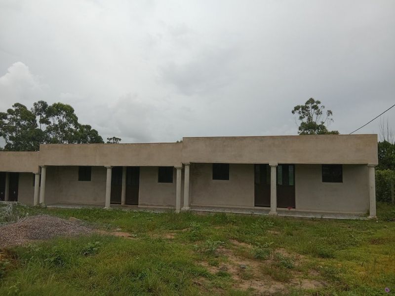 Exterior view of a single-story building featuring a covered veranda with concrete columns and unfinished exterior wall surfaces.