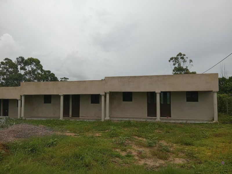 Exterior view of a single-story building featuring a covered veranda with concrete columns and unfinished exterior wall surfaces.