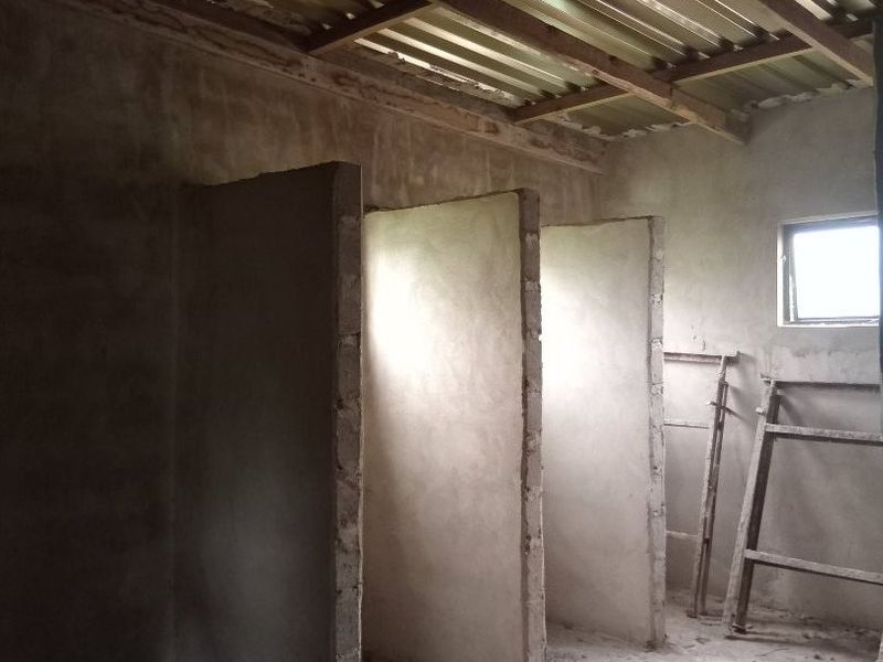 An unfinished utility space featuring exposed corrugated metal roofing, timber trusses, and masonry partition walls, currently in a shell condition.