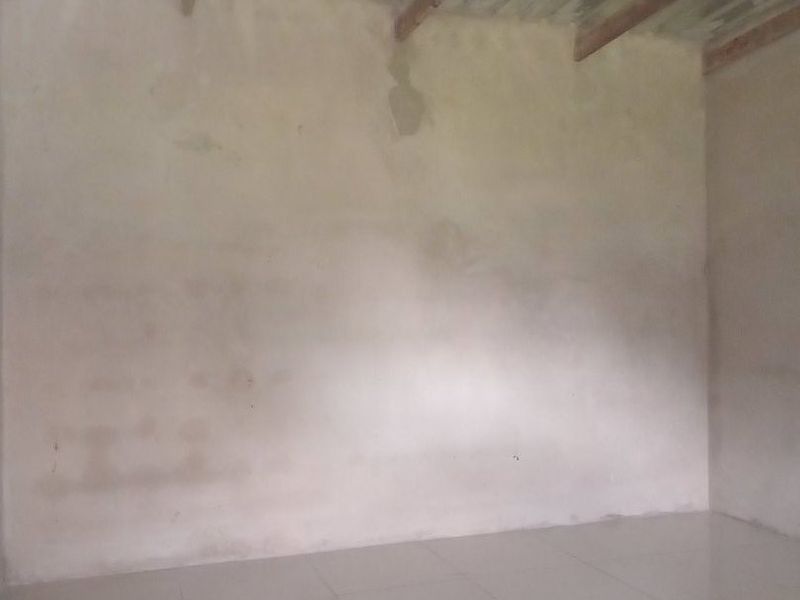 An unfinished interior space featuring tiled flooring, exposed timber rafters, and corrugated metal roof sheeting, awaiting final wall finishes and ceiling installation.
