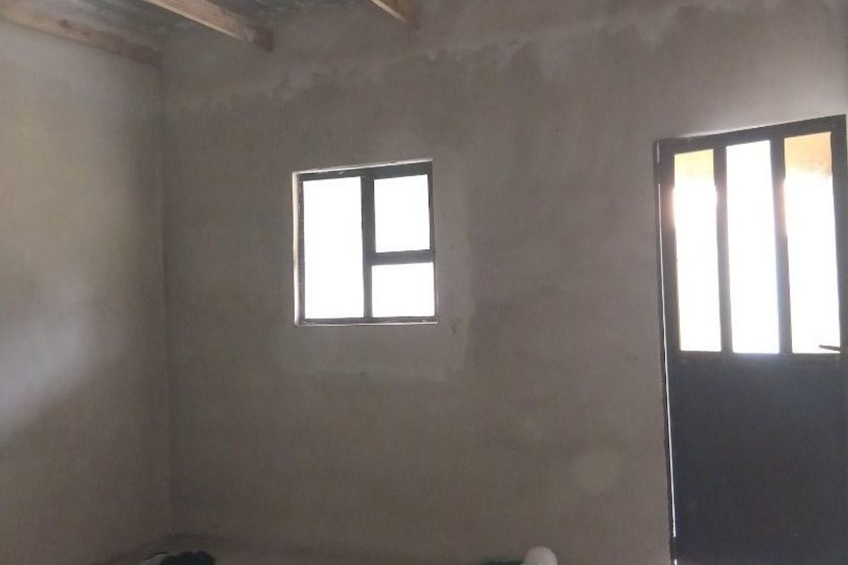 An unfinished interior space featuring tiled flooring, exposed timber roof trusses, and a corrugated metal ceiling, awaiting final plastering and finishing.