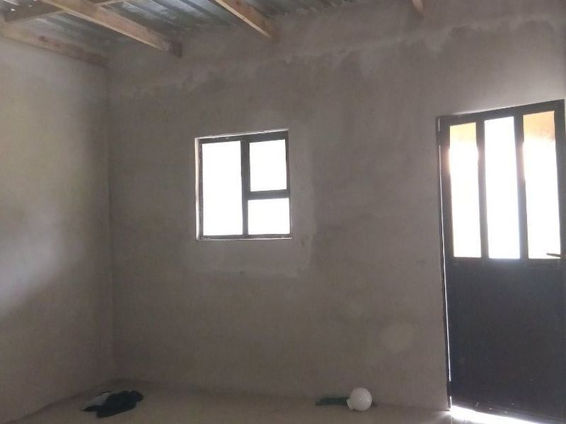 An unfinished interior space featuring tiled flooring, exposed timber roof trusses, and a corrugated metal ceiling, awaiting final plastering and finishing.