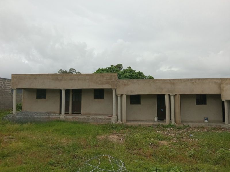 Rear view of a single-story residential building featuring a covered veranda with concrete columns and unfinished exterior wall surfaces.