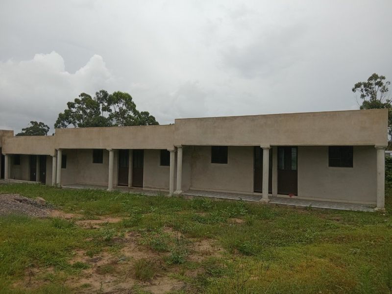Exterior view of a single-story apartment block featuring a covered veranda with concrete columns and unfinished exterior wall surfaces.