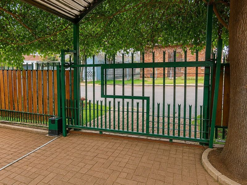 Secure front entrance featuring a paved driveway, metal carport, and automated sliding steel gate with perimeter fencing.