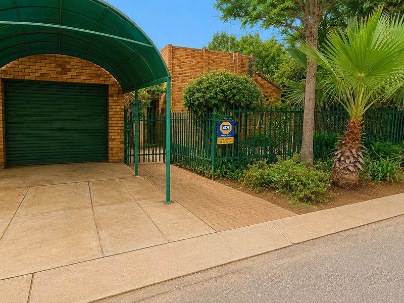 Front exterior view featuring a brick facade, a covered carport, a roller garage door, and secure metal fencing with a pedestrian gate.