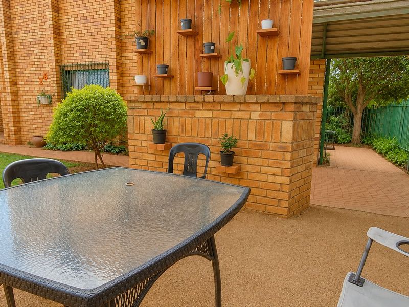 A covered outdoor patio area featuring a brick wall, timber privacy screen, and paved walkway, providing a functional space for outdoor relaxation.