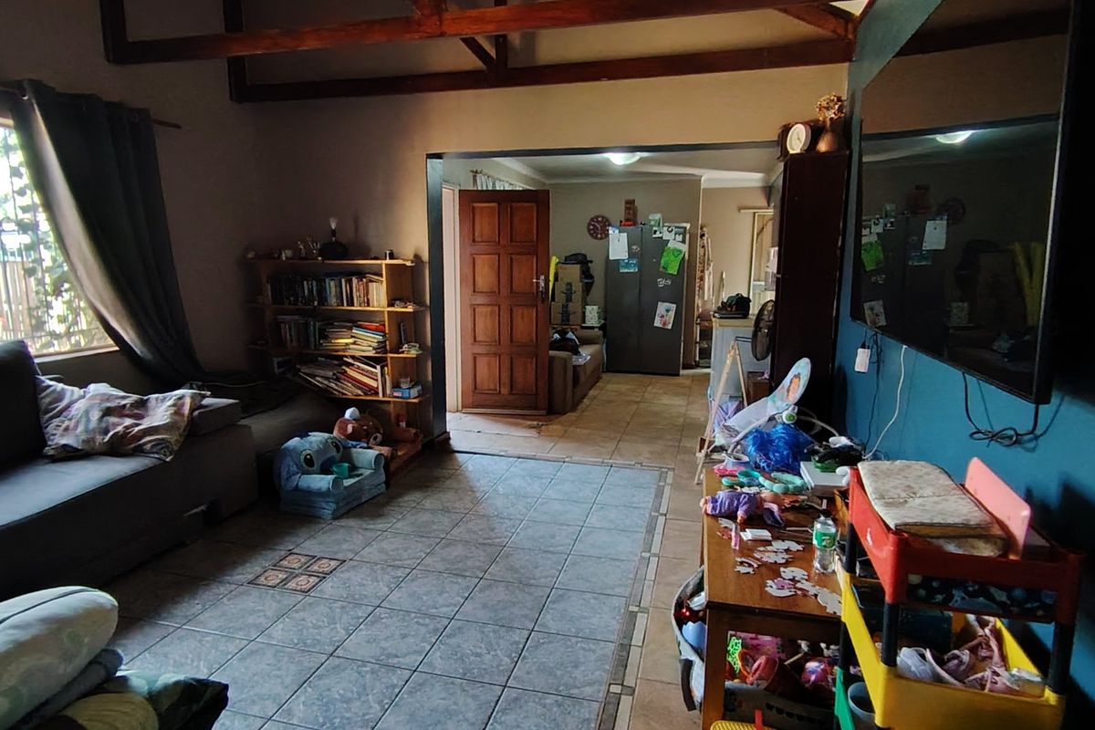 A living room featuring tiled flooring and exposed timber ceiling beams, providing a functional space with direct access to the home's entrance area.