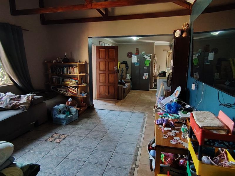 A living room featuring tiled flooring and exposed timber ceiling beams, providing a functional space with direct access to the home's entrance area.