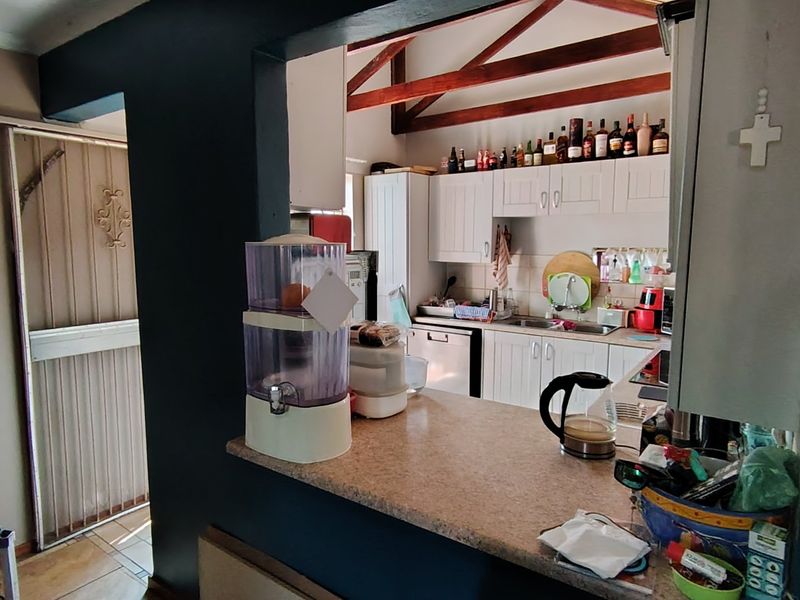A functional kitchen featuring white cabinetry, stone countertops, and exposed timber roof trusses, with a convenient pass-through window overlooking the adjacent living area.