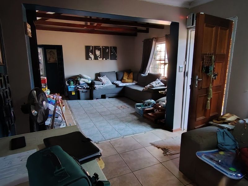 Open plan living area featuring tiled flooring and exposed timber ceiling beams, providing a connected space between the main living zones.
