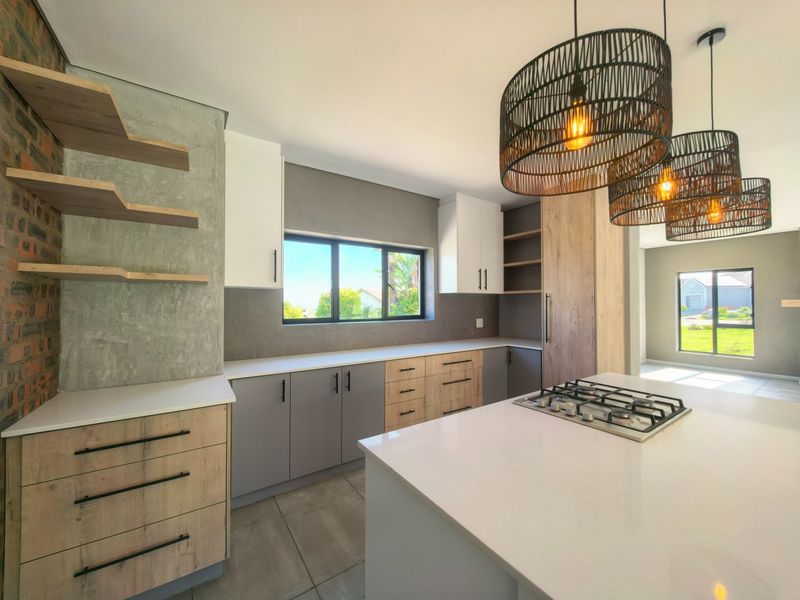 Modern kitchen featuring a central island with gas cooktop, stone countertops, two-tone cabinetry, exposed brick accents, and stylish pendant lighting.