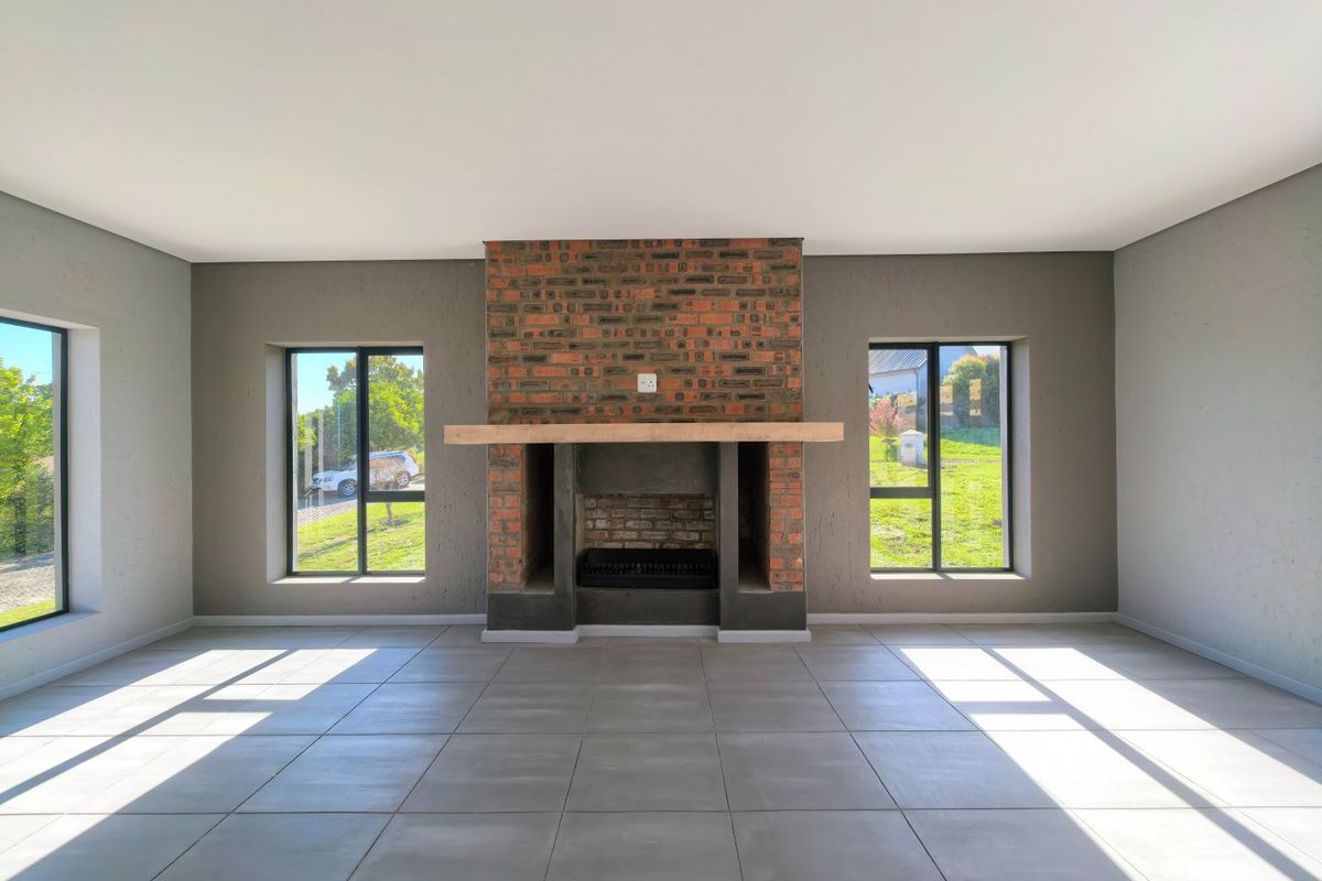 Spacious living room featuring a central exposed brick fireplace with a timber mantelpiece, large windows, and neutral tiled flooring.