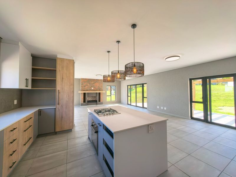 Spacious open-plan kitchen and living area featuring a central island with gas hob, brick fireplace, and large sliding doors leading to the garden.