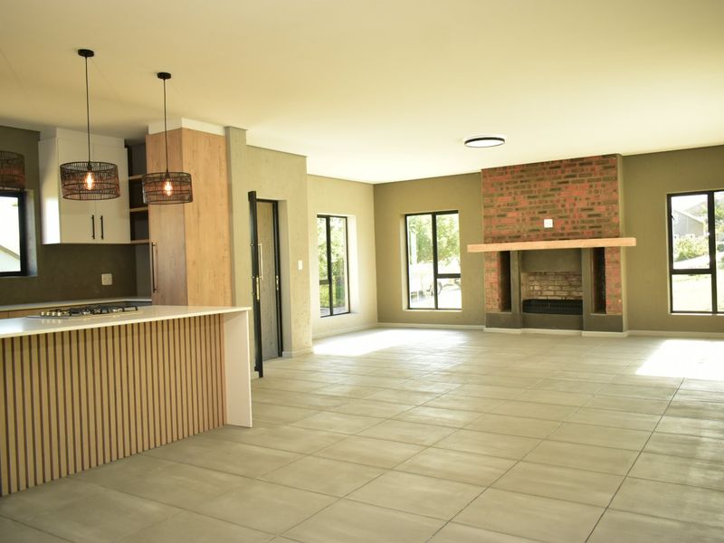 Spacious open-plan living area featuring a modern kitchen with island, tiled floors, and a characterful brick fireplace with a timber mantelpiece.