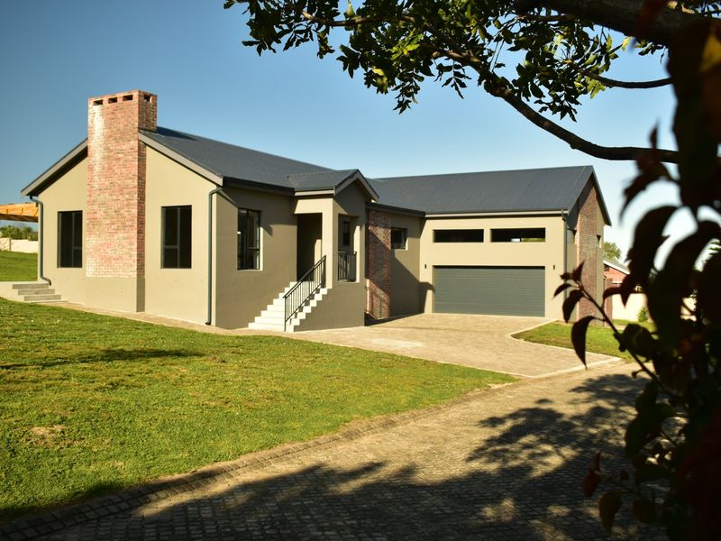 A modern single-story house featuring a prominent brick chimney, metal roofing, an attached garage, and a paved driveway set on a landscaped lawn.