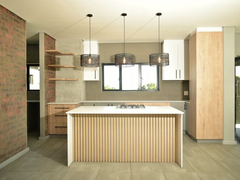 Modern kitchen featuring a central island with a gas hob, sleek cabinetry, exposed brick accents, and stylish pendant lighting.
