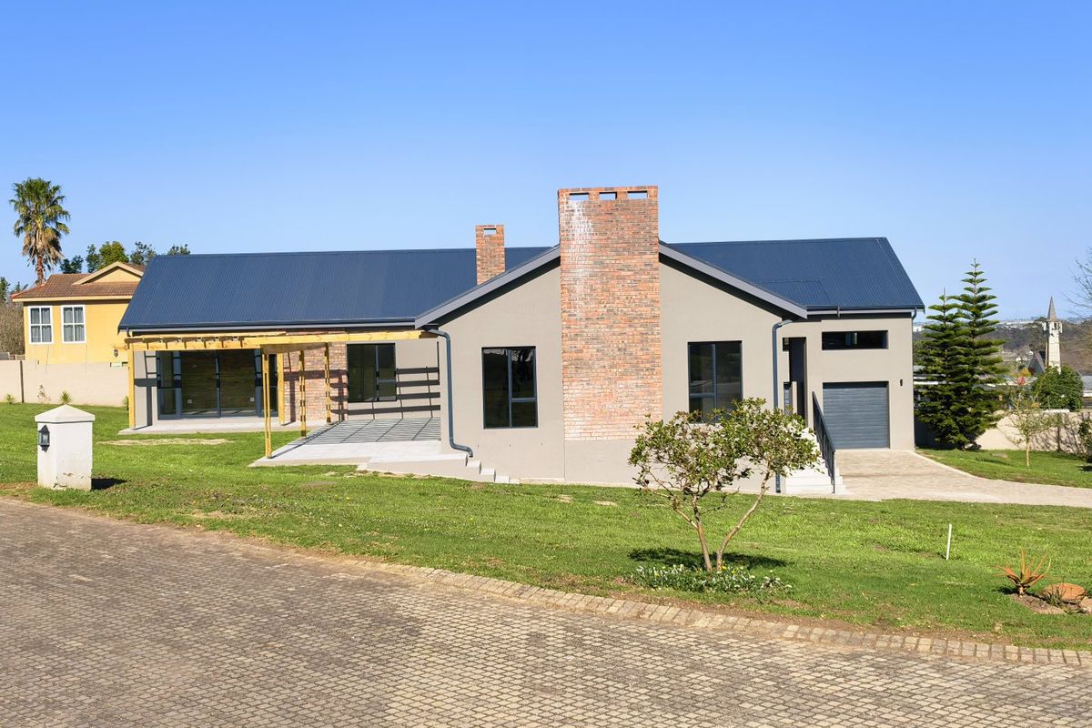 A modern single-story house featuring a brick chimney, metal roof, timber pergola, and a paved patio area set within a landscaped garden.