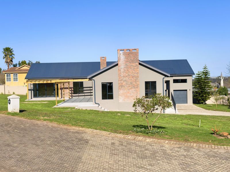 A modern single-story house featuring a brick chimney, metal roof, timber pergola, and a paved patio area set within a landscaped garden.