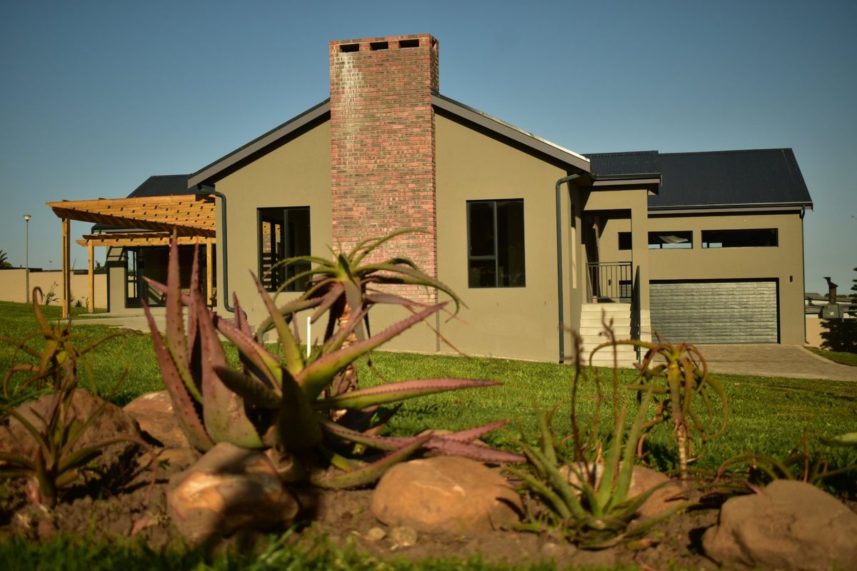 Rear view of a modern house featuring a prominent brick chimney, attached timber pergola, and integrated garage with a paved driveway.