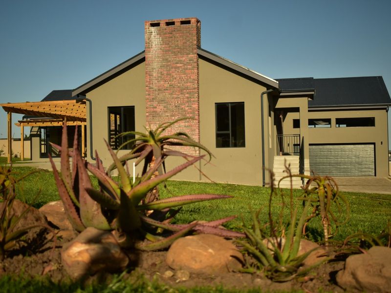 Rear view of a modern house featuring a prominent brick chimney, attached timber pergola, and integrated garage with a paved driveway.