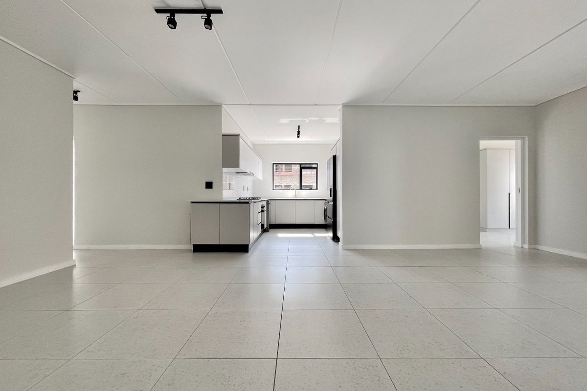 A spacious, modern open-plan living and kitchen area featuring neutral tiled flooring, contemporary cabinetry, and integrated appliances in a clean, minimalist setting.