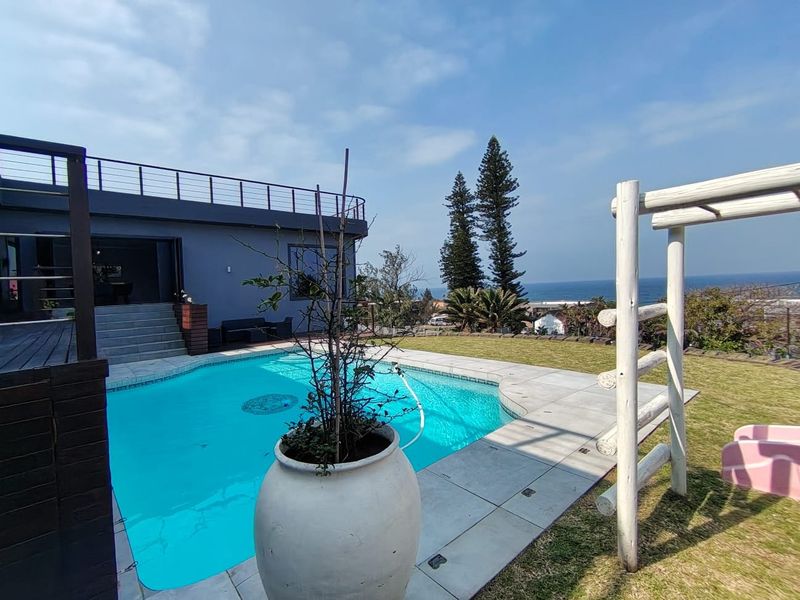 Outdoor pool area featuring a swimming pool, paved surround, timber decking, and a lawn with ocean views.