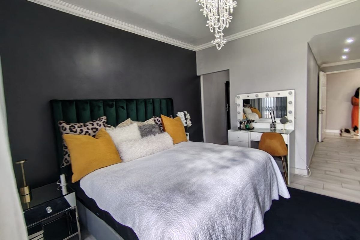 A well-maintained bedroom featuring crown molding, recessed lighting, and tiled flooring, accented by a dark feature wall and a crystal chandelier.