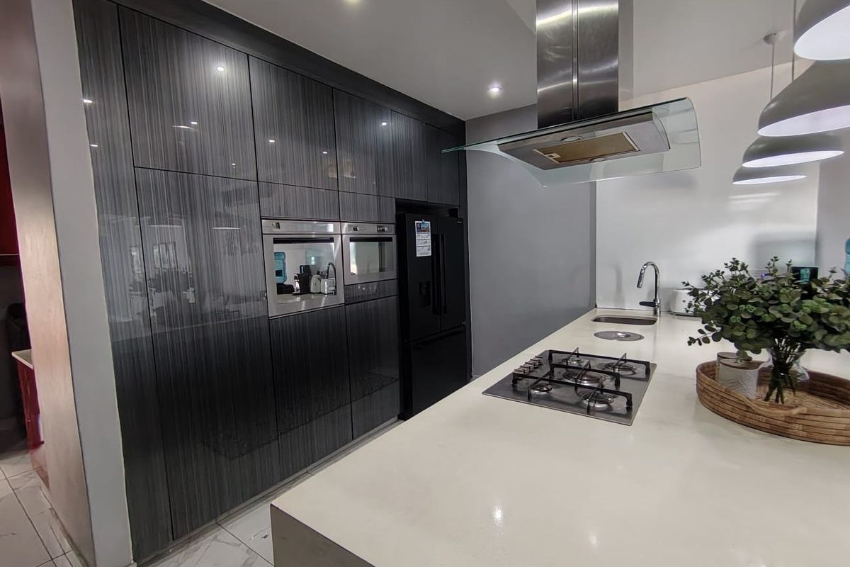 Modern kitchen featuring high-gloss dark cabinetry, stone countertops, a central island with a gas cooktop, and integrated stainless steel appliances.